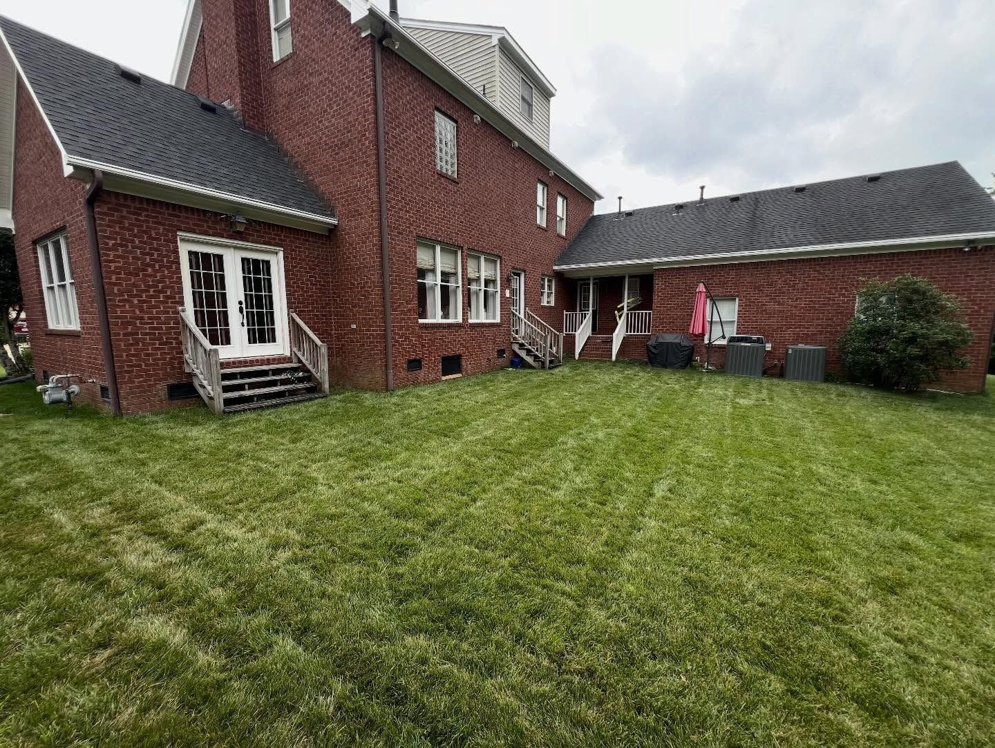 Backyard with green lawn, brick house, white patio door, and overcast sky