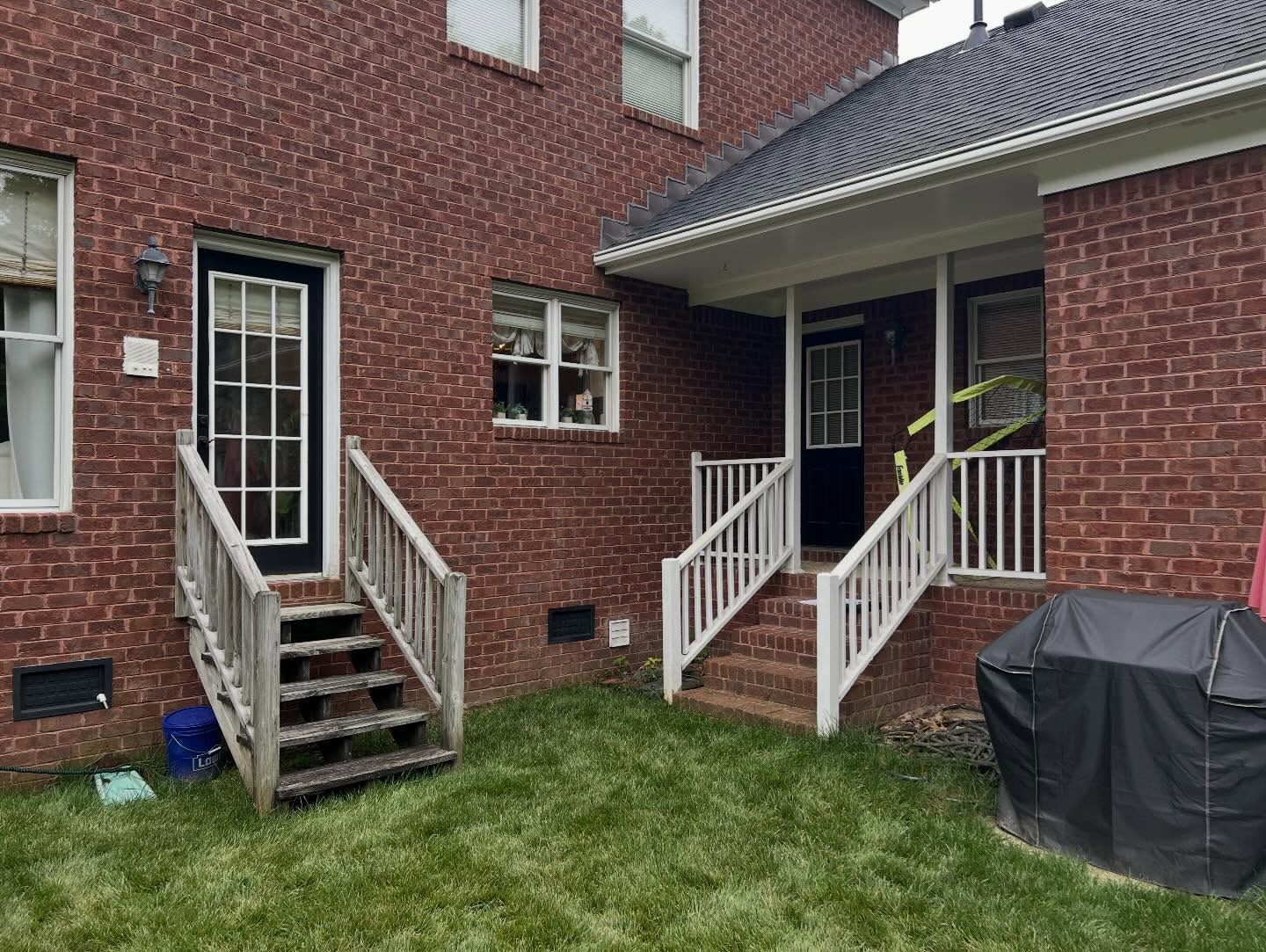 Brick townhouse back entrance with two white-railed stairways, grassy yard, and a covered grill.