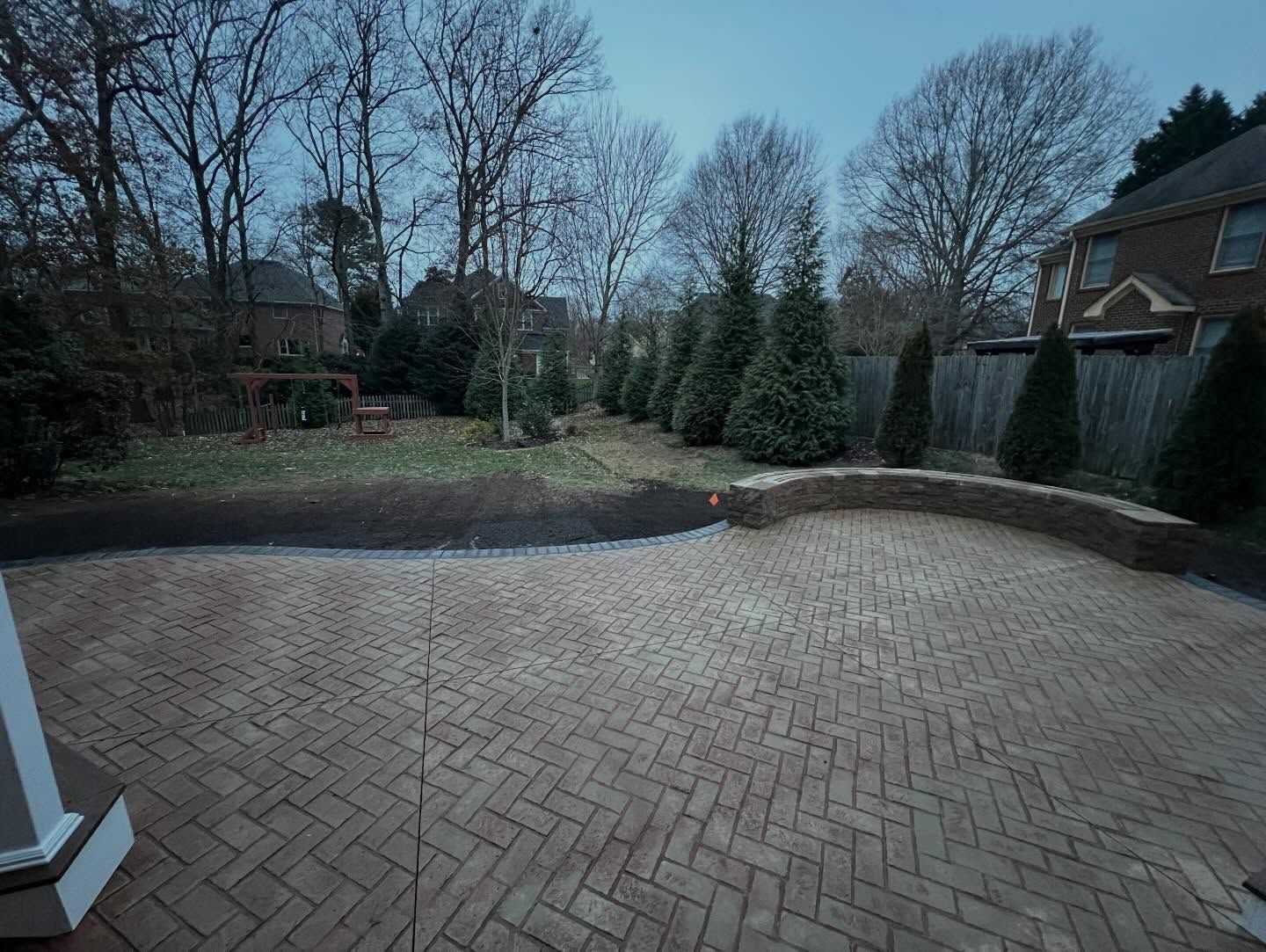 Brick patio overlooking a landscaped backyard with trees and evergreens at dusk