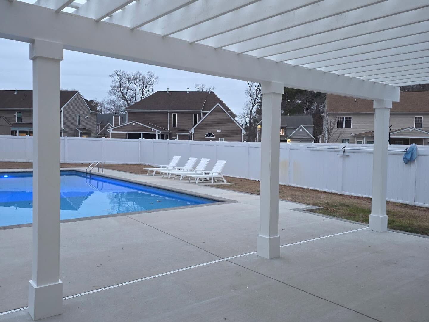 Covered patio overlooking a backyard pool and white fence, with lounge chairs in the distance.