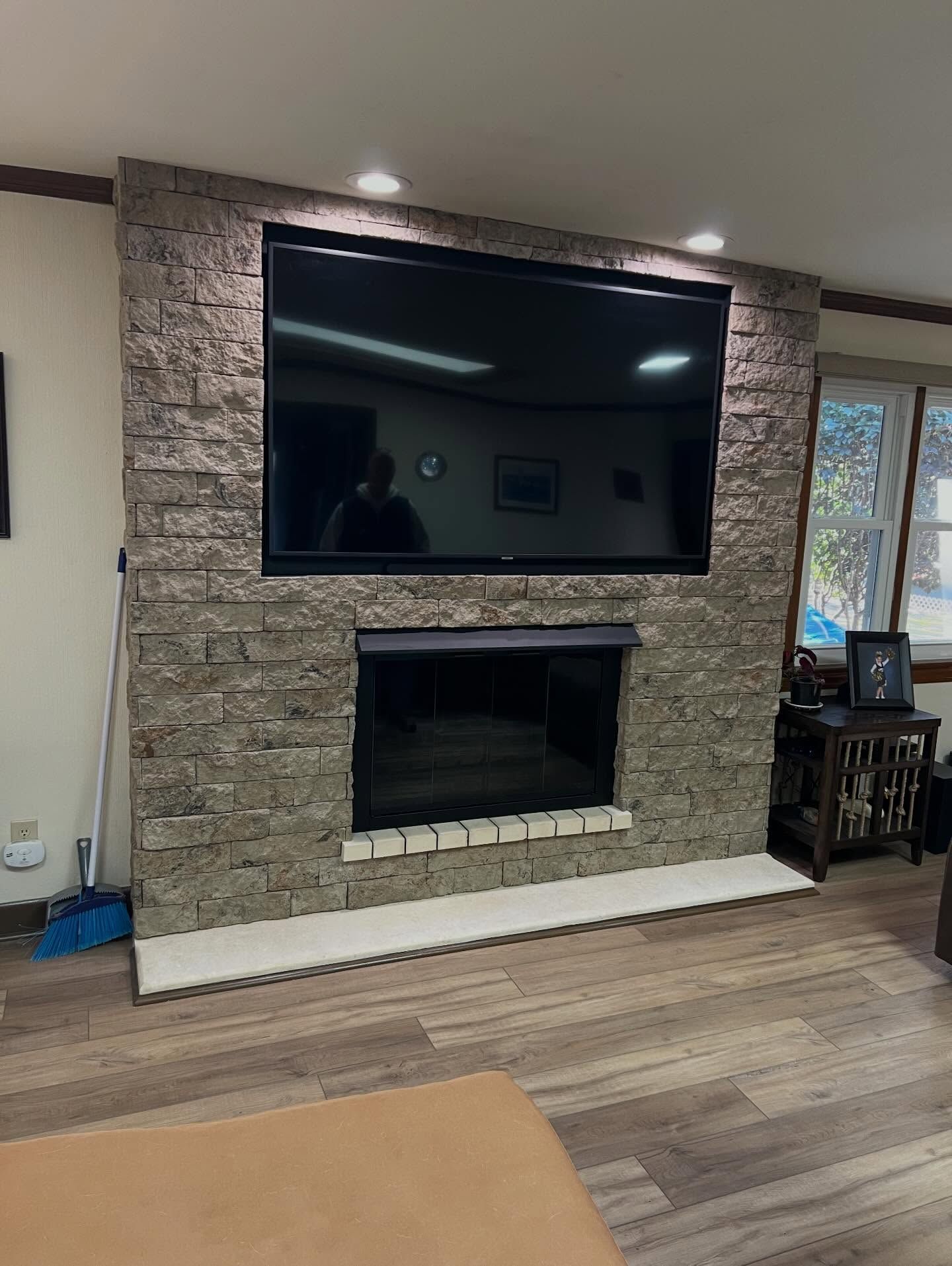 Stone fireplace wall with large TV above and open firebox below in a living room