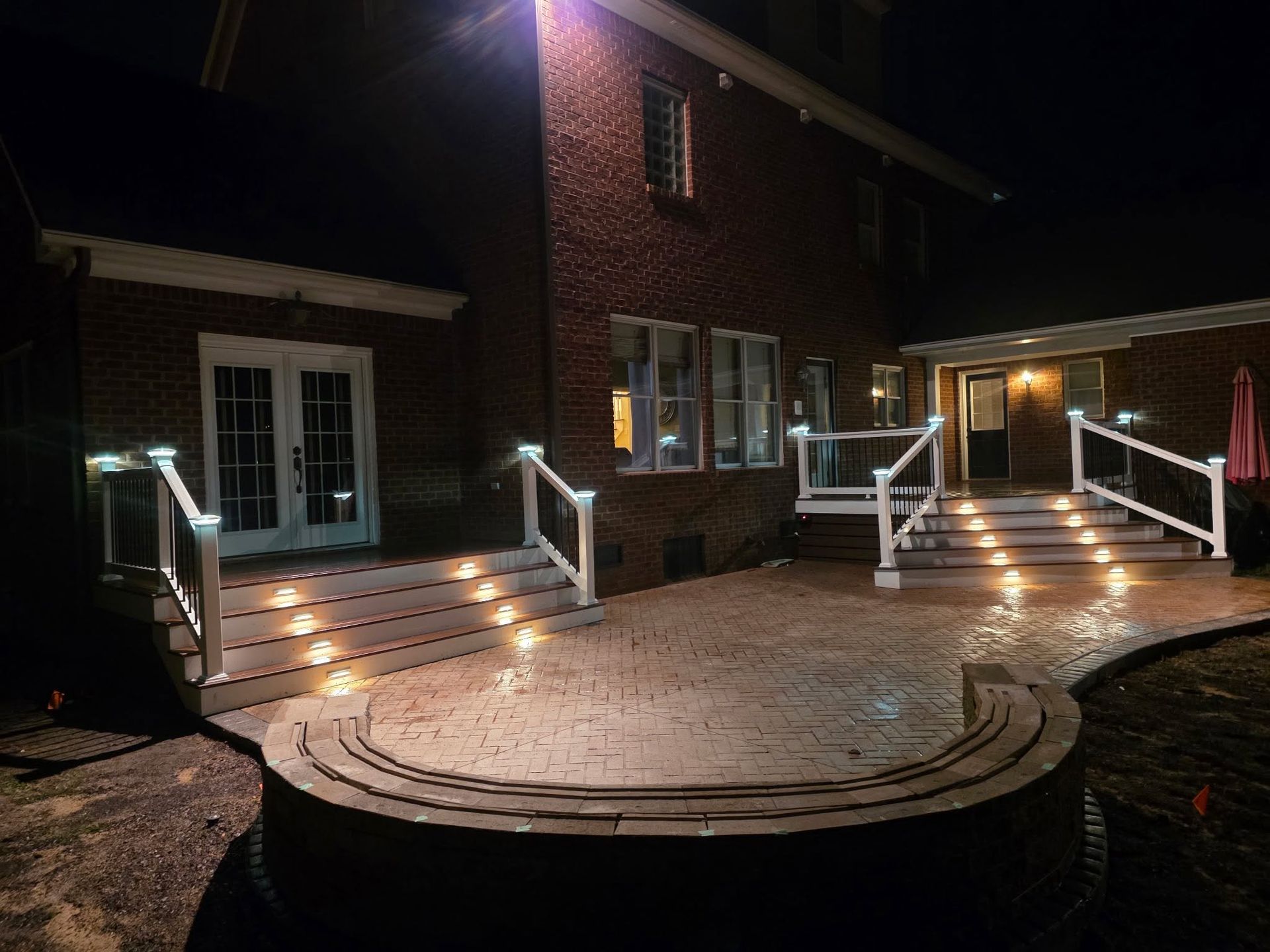 Nighttime brick house with lit steps, railings, and a circular patio in front