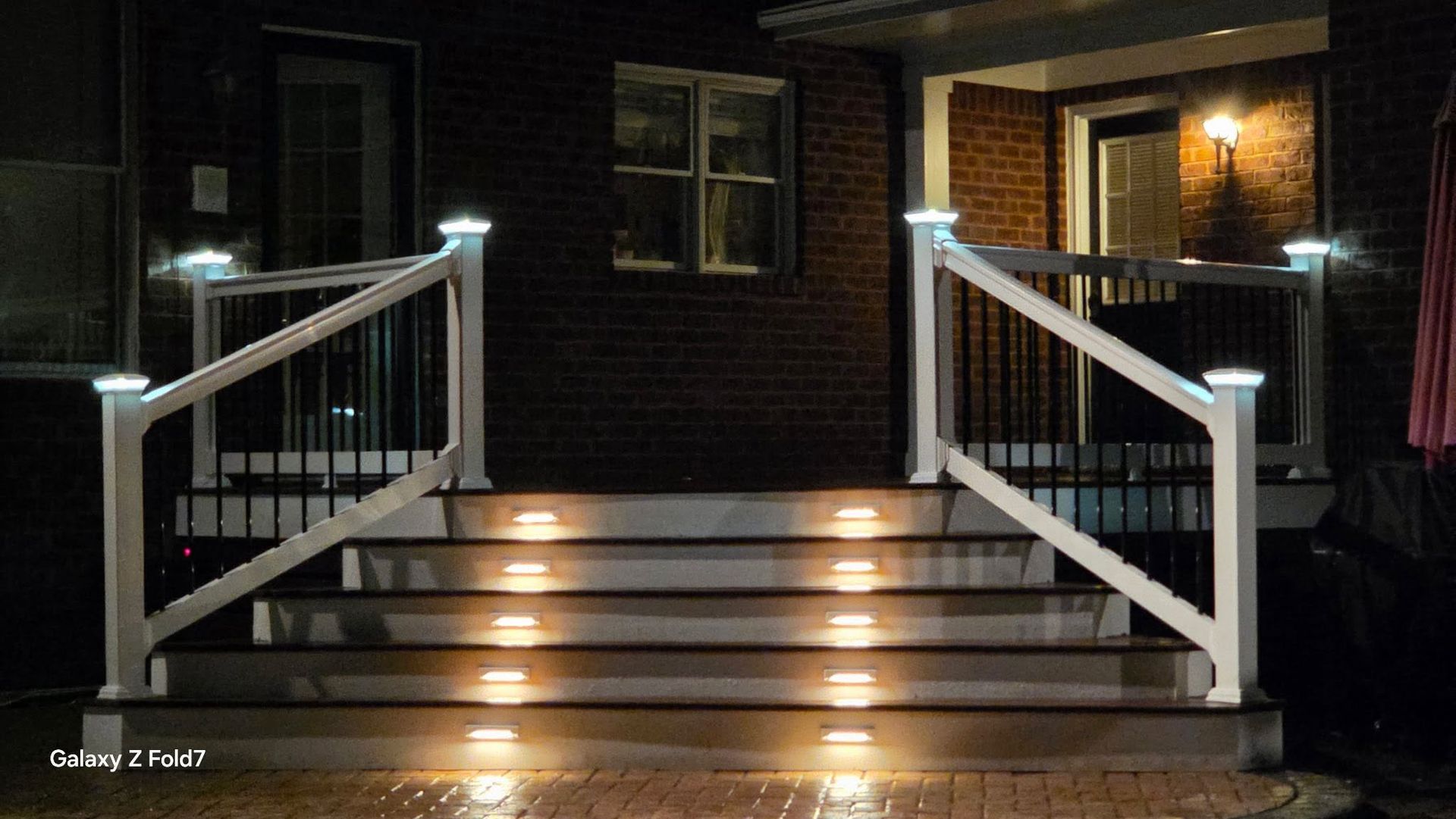 Front porch steps with white railings and lit stair lights at night, leading to a brick house entrance