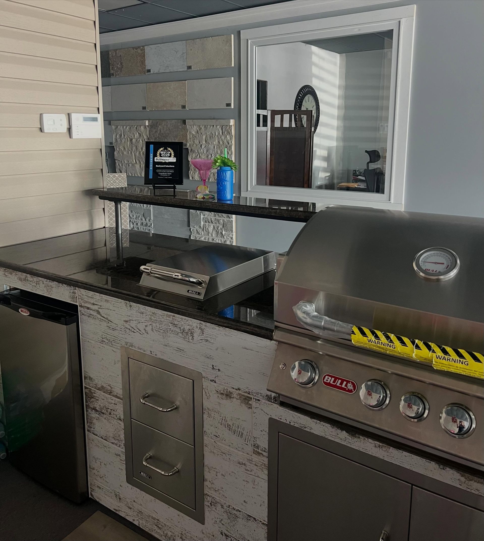 Outdoor kitchen with stainless grill, sink, and bar counter in a covered patio area