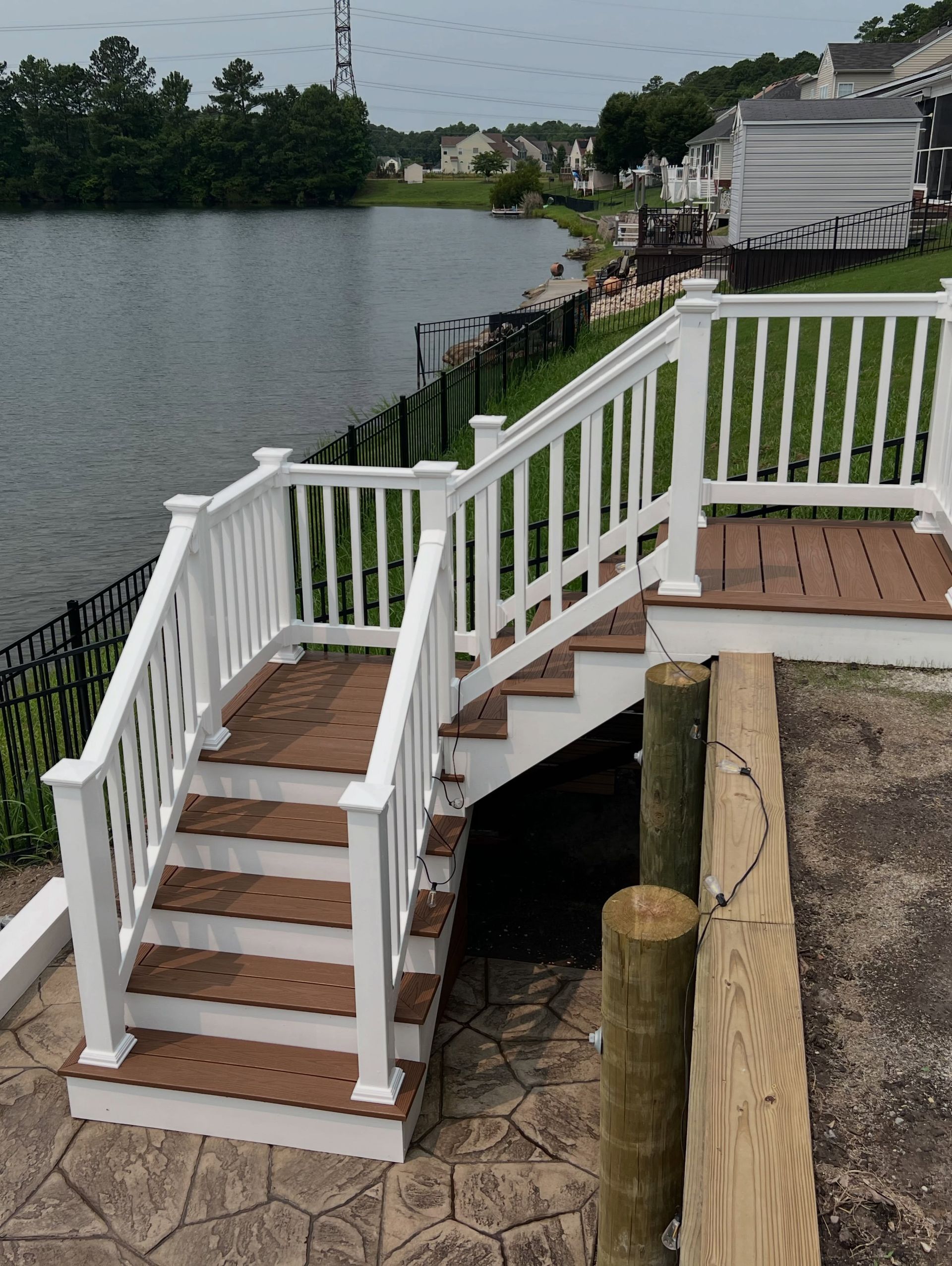 White-railed wooden stairs descending to a lakeside dock beside calm water and houses