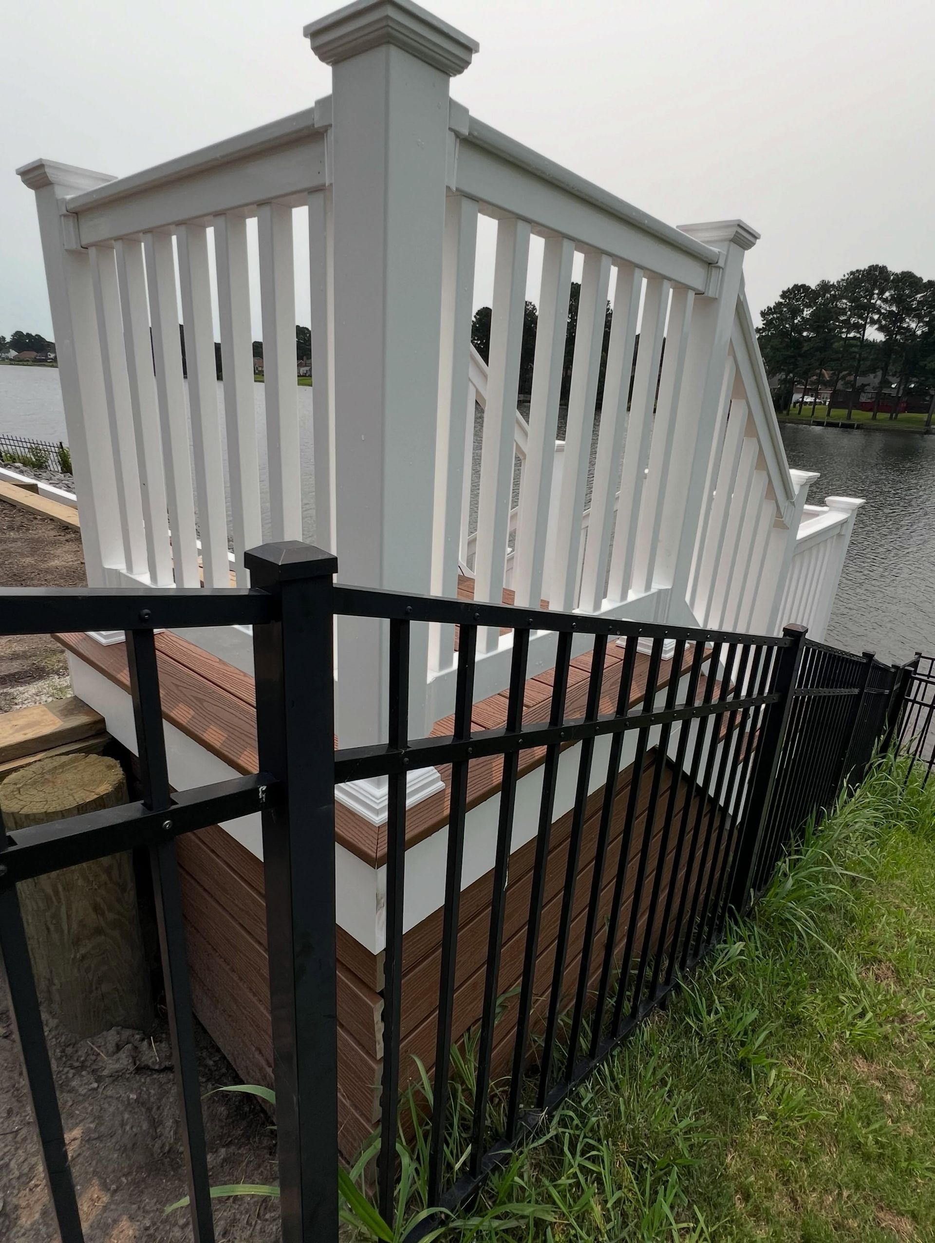 Black metal fence in front of white porch railing beside a brick foundation and grassy yard
