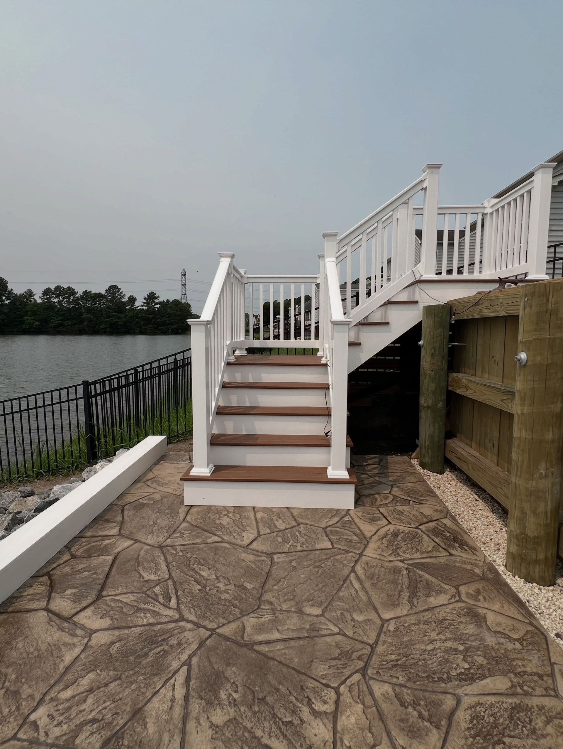 White wooden stairs beside a waterfront deck, with a stone patio and lake view