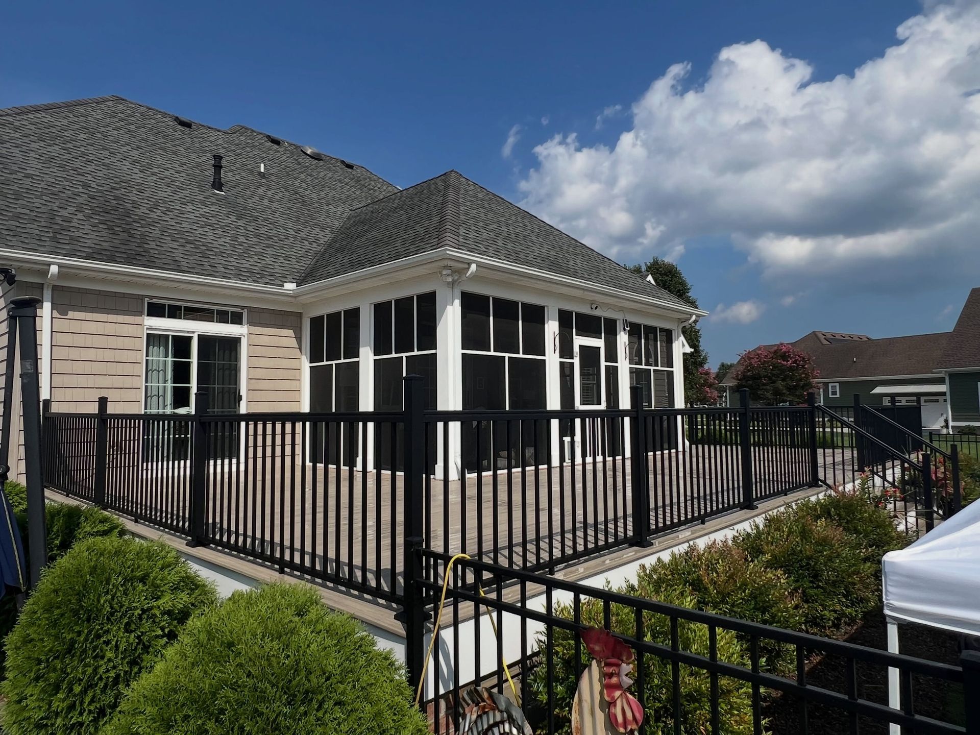 Suburban house with screened porch, black metal railing, and landscaped front yard under a cloudy sky
