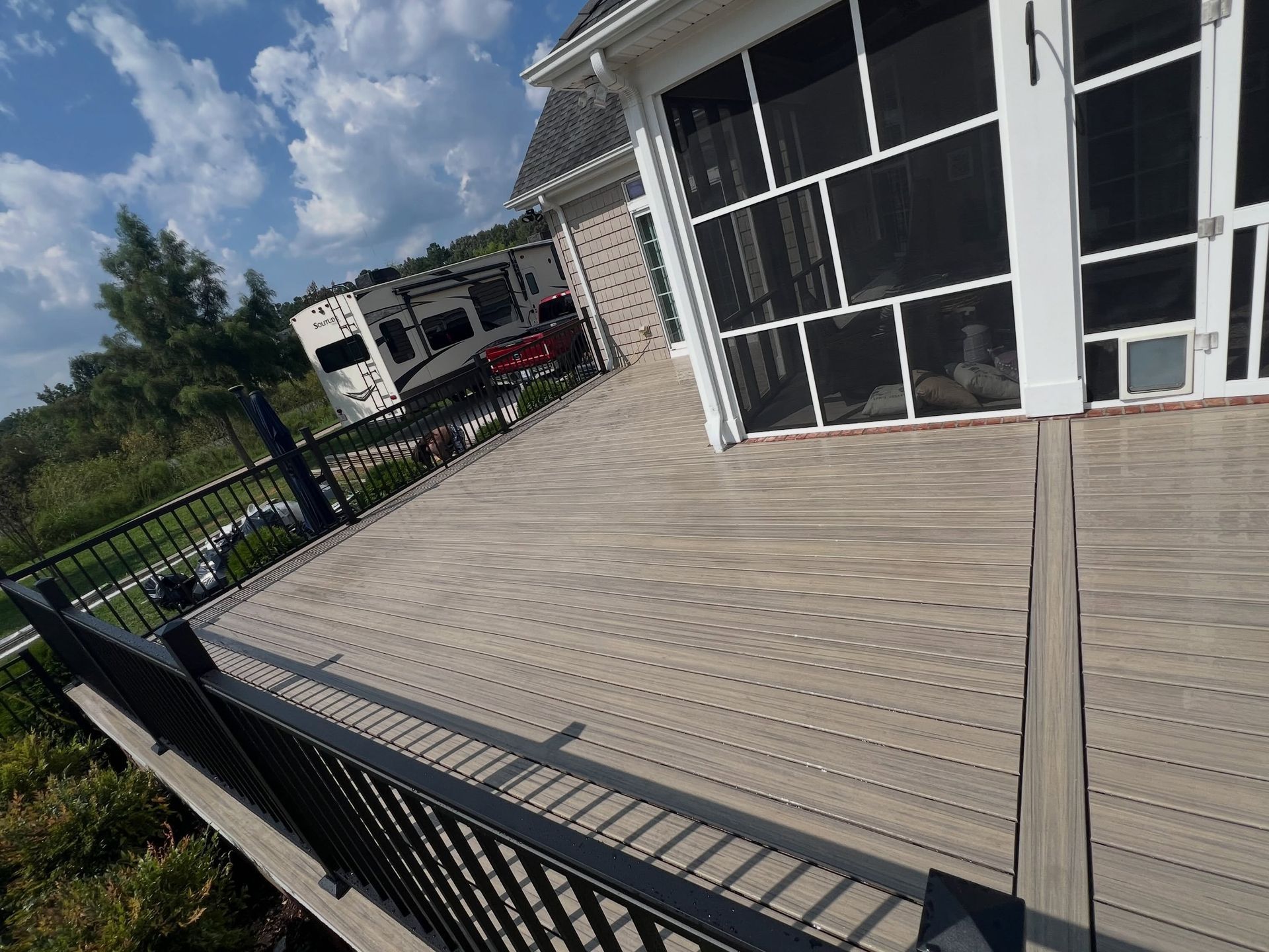 Wooden deck beside a screened porch, with a black railing and cloudy sky in the background.
