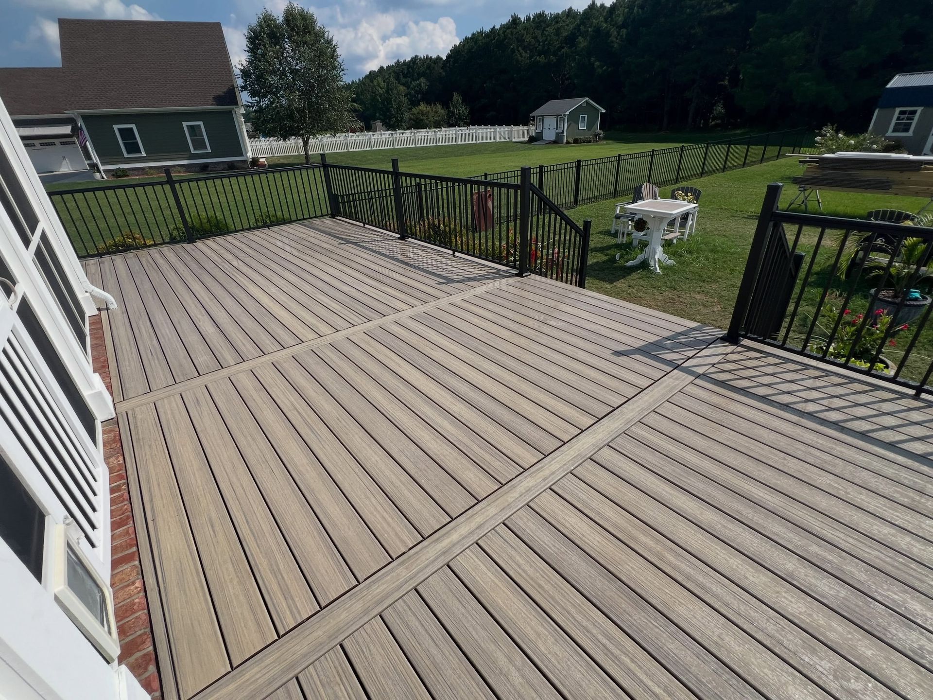 Spacious tan wooden deck with black railings overlooking a grassy backyard and white picnic table