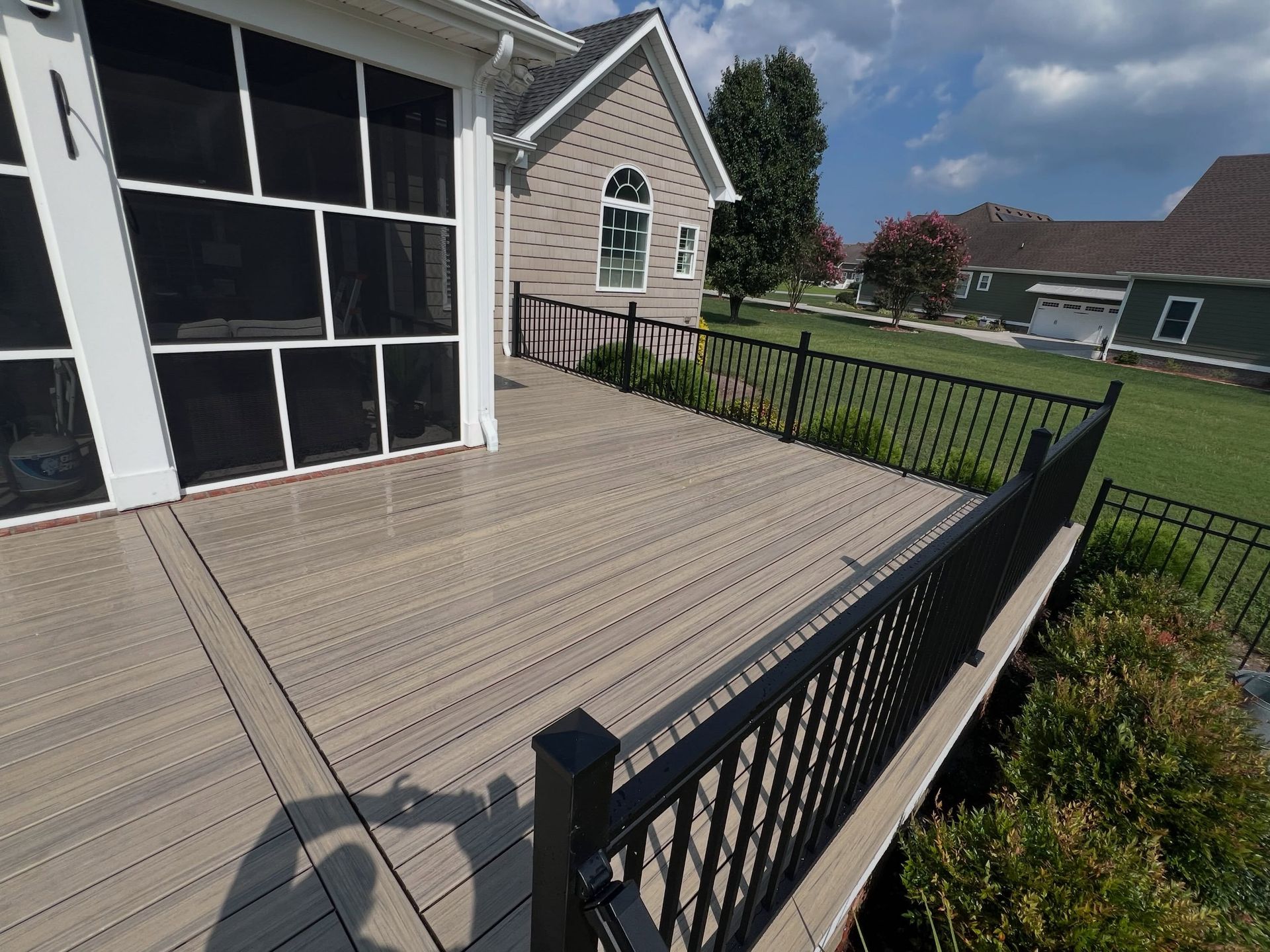 Backyard wooden deck with black metal railing beside a house, overlooking a grassy yard