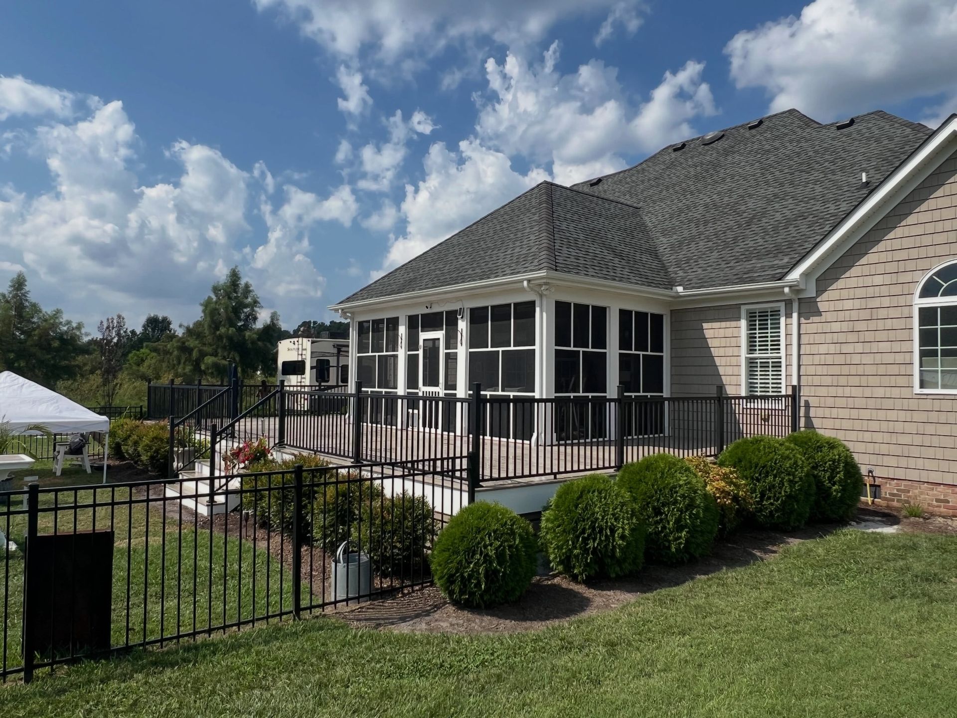 Brick house with screened porch, black metal fence, and manicured lawn under a partly cloudy sky