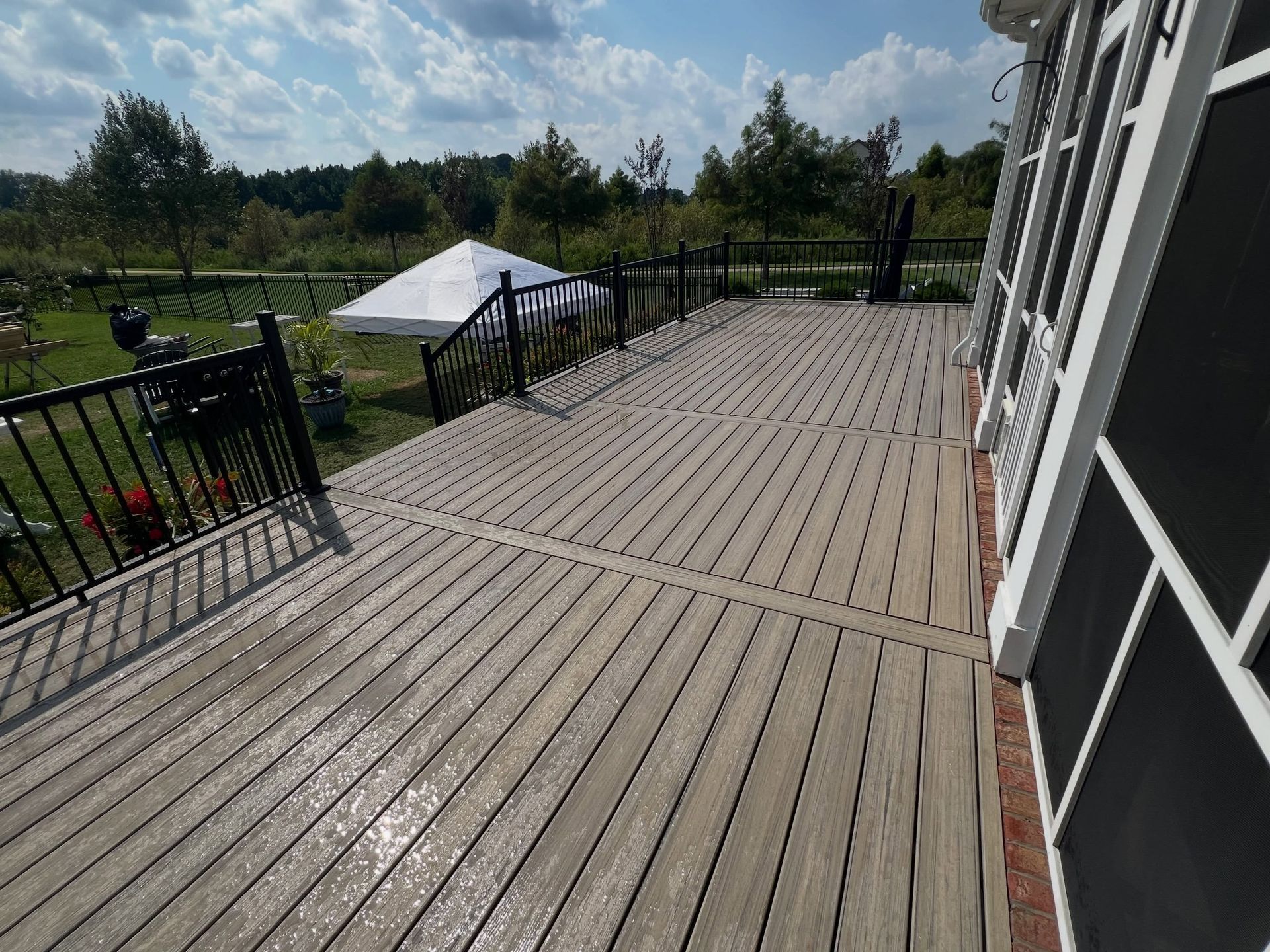 Wooden deck with black railings beside a house, overlooking a green yard under a cloudy sky