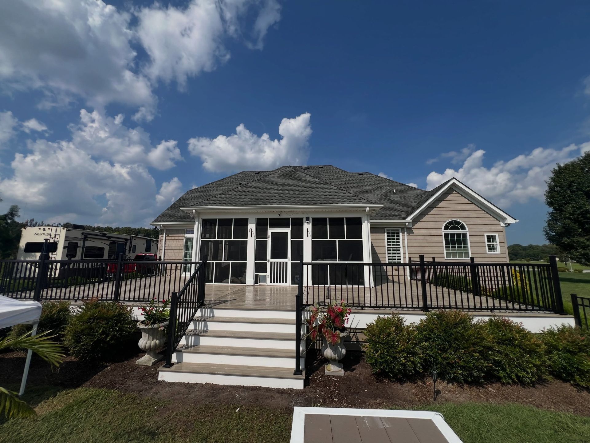 White house with front porch and steps, surrounded by a fenced yard under a partly cloudy blue sky