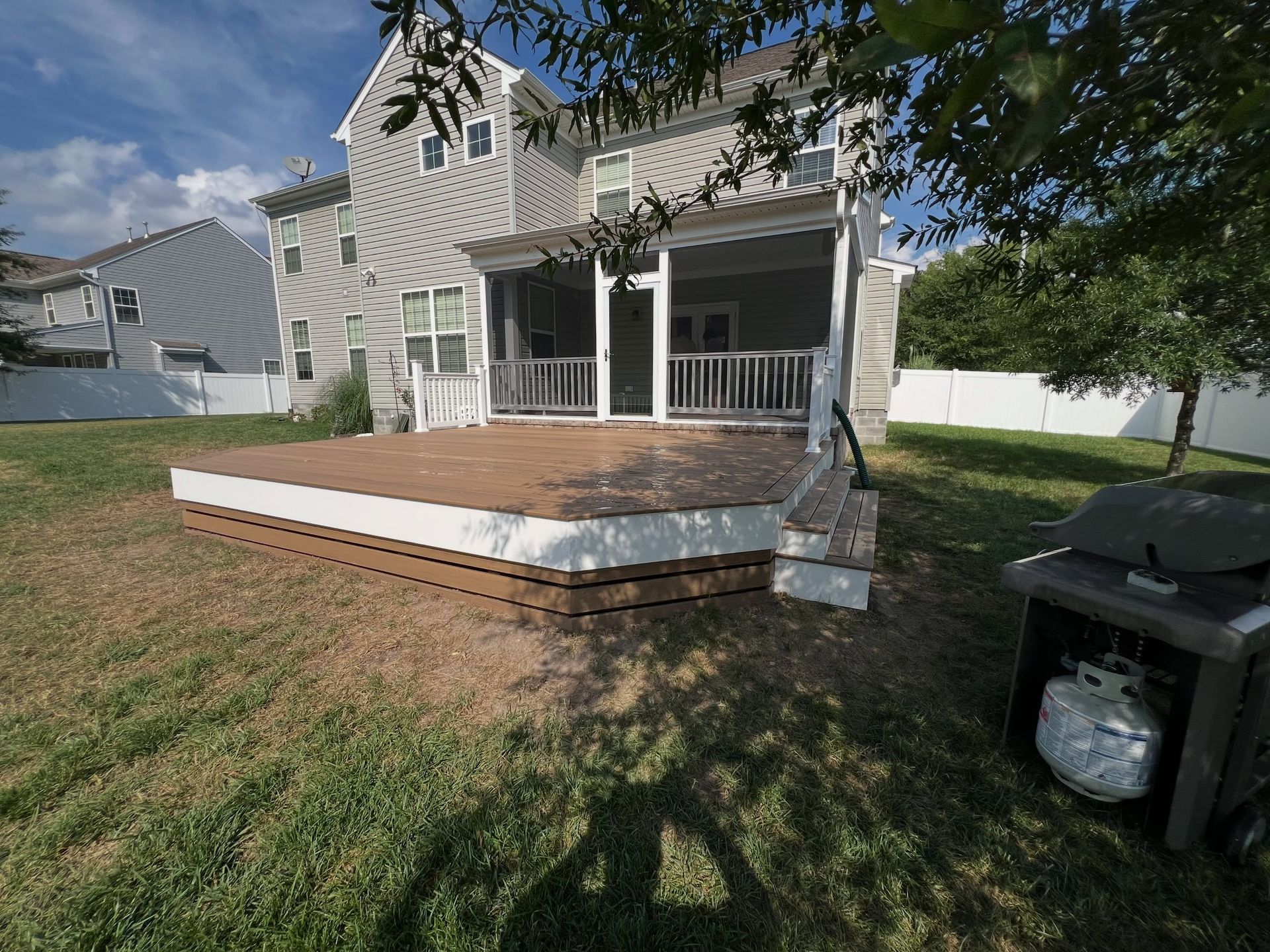 Backyard deck with wooden porch, white railing, and steps beside a house and lawn