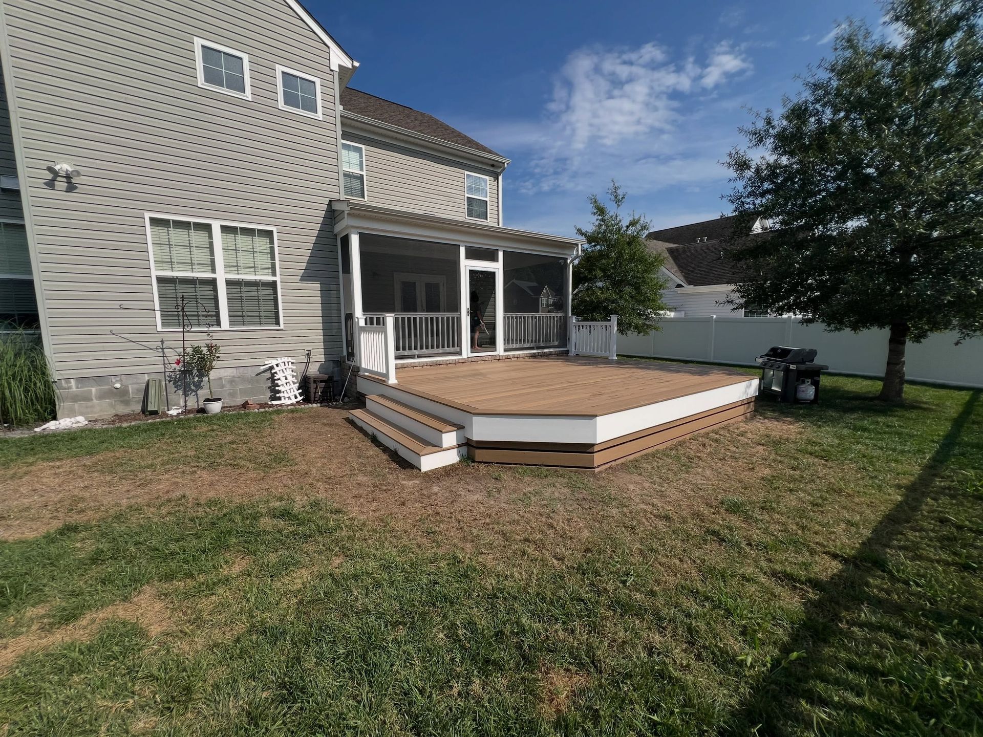 Backyard deck with white railing and steps beside a beige house under a blue sky