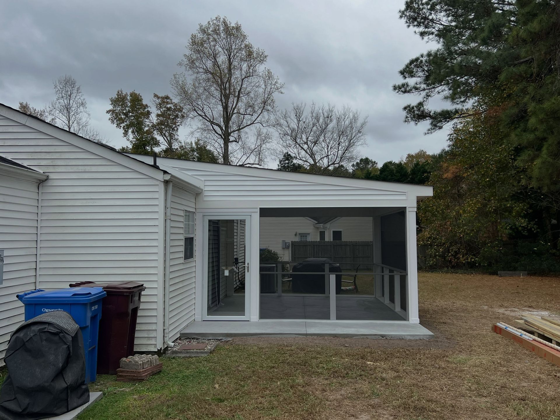 White house exterior with a screened-in patio enclosure and blue trash bins by the side yard.