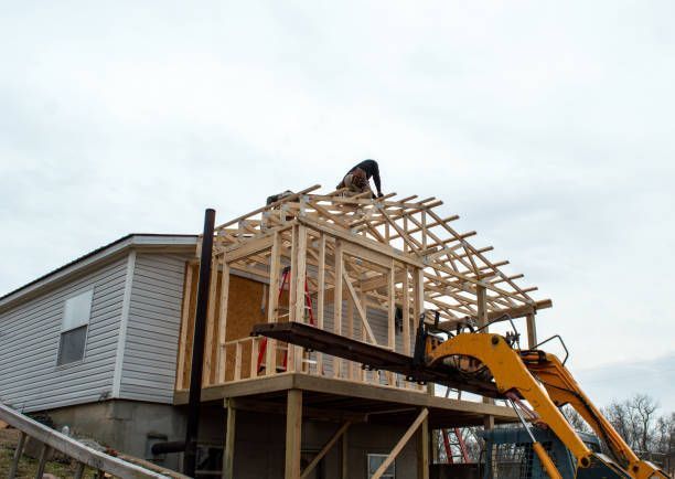Construction workers framing a house addition on a deck, assisted by a forklift.