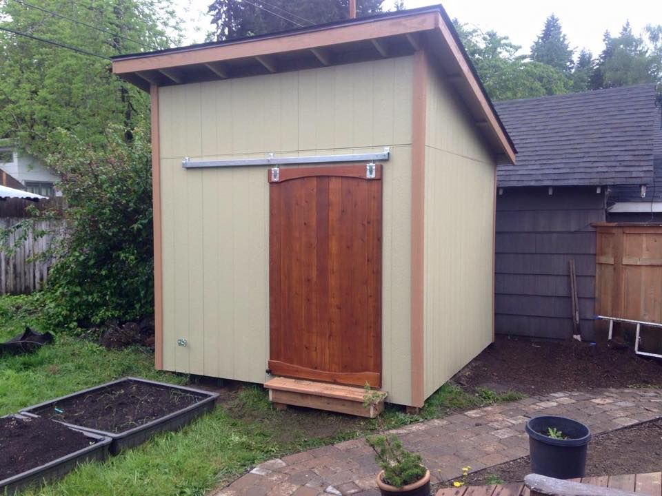 Tan shed with brown door, set in a backyard with a stone pathway.