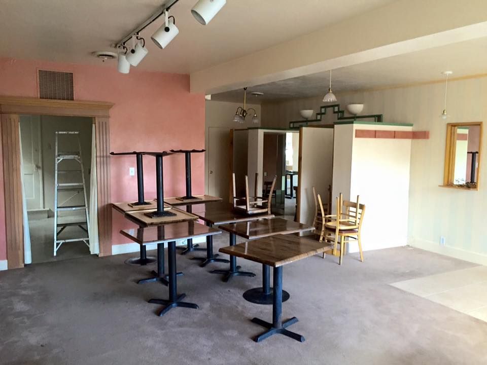 Empty commercial space with tables and chairs, pink and beige walls, overhead lighting.