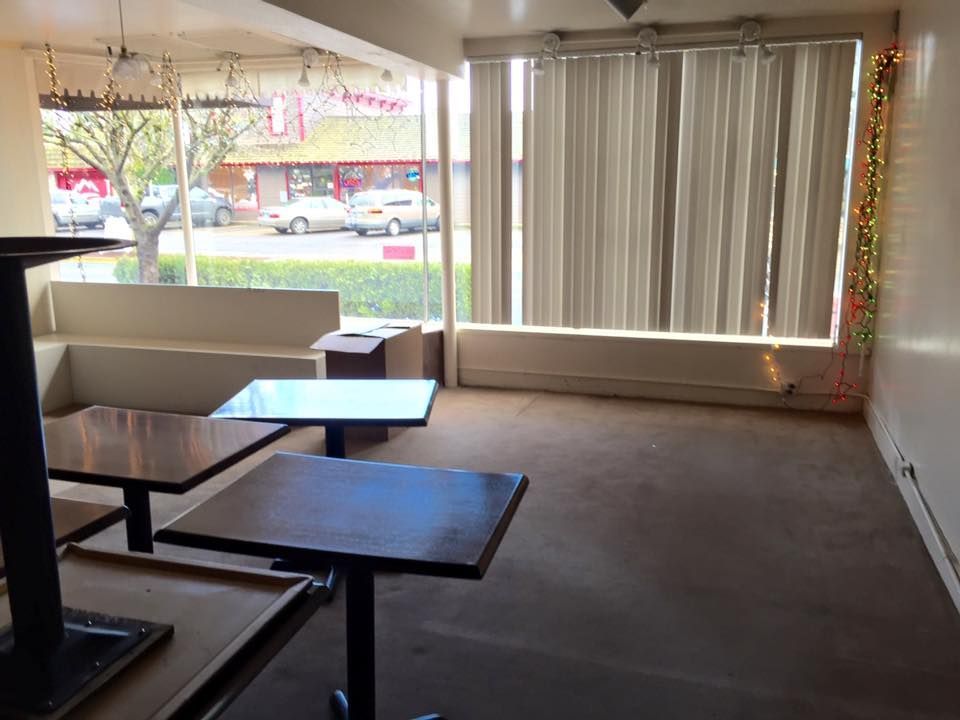 Empty restaurant interior with tables, windows, and light-colored curtains. Outdoor view visible.