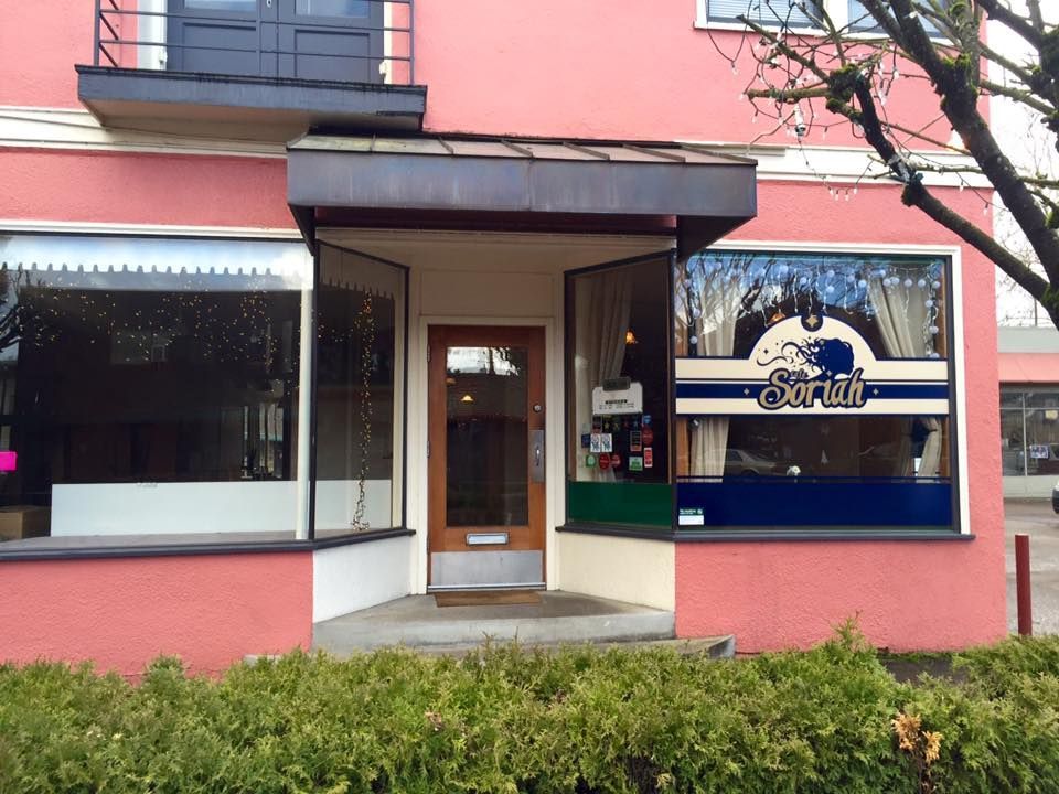 Pink building with storefront; blue and white sign, open door, bushes in front.