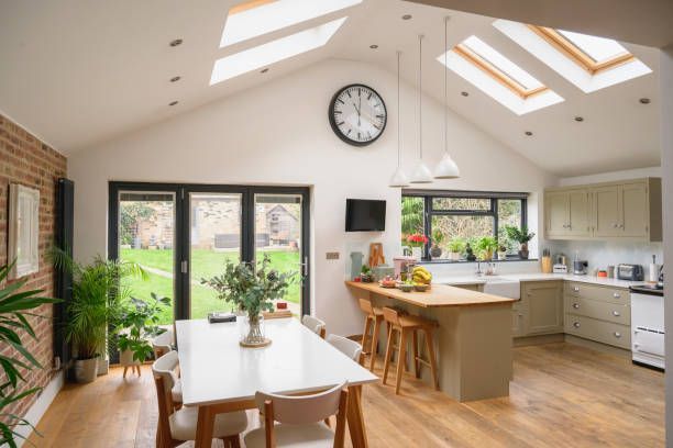 Spacious kitchen with skylights, dining table, and island bar, overlooking a garden through large glass doors.