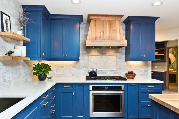 Blue kitchen with wood range hood, white countertops, and floating shelves.