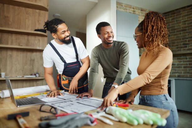 Three people, a couple and a contractor, review house plans together, smiling.