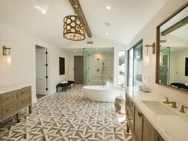 Spacious, bright bathroom with patterned tile floor, white tub, glass shower, double sink, and decorative lighting.