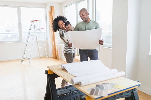 Family looking at blueprints in a bright, empty room with a ladder, planning a home renovation.