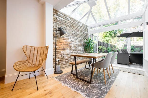 Dining room with a glass roof, brick wall, table, chairs, and a wicker chair.