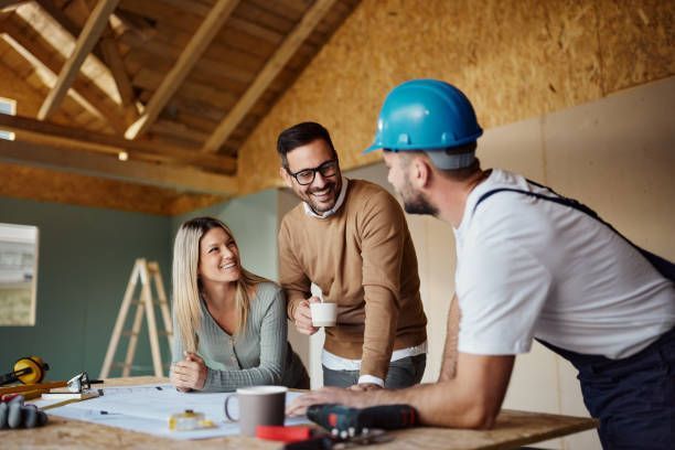 A couple consults with a construction worker at a worksite, looking at blueprints.