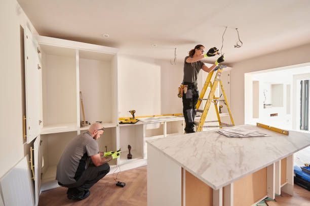 Two people installing kitchen cabinets; one on ladder, one kneeling.