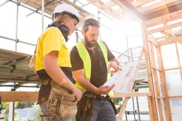 Two construction workers, one female, looking at blueprints on a construction site.