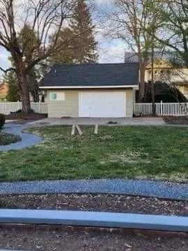 Tan garage with white door, black roof, and small lawn in front.