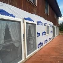 Exterior view of a house with windows covered in blue tarp, next to a wooden deck.