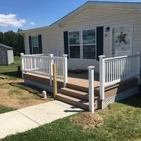 A tan house with a deck and white railing, under a blue sky.