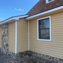 Beige siding on a house with a window and a stone wall section, against a blue sky.