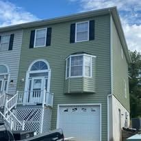 Green-sided two-story home with a garage. Features bay window, white trim, and a blue sky.