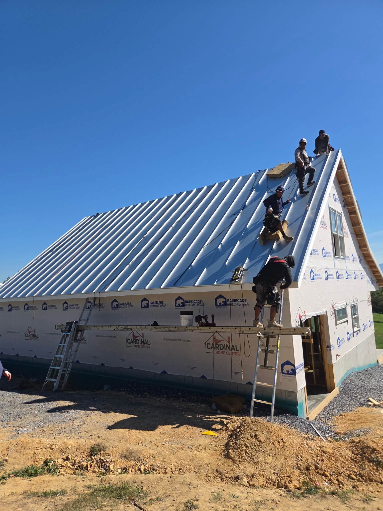 Workers installing a blue metal roof on a small white house under construction