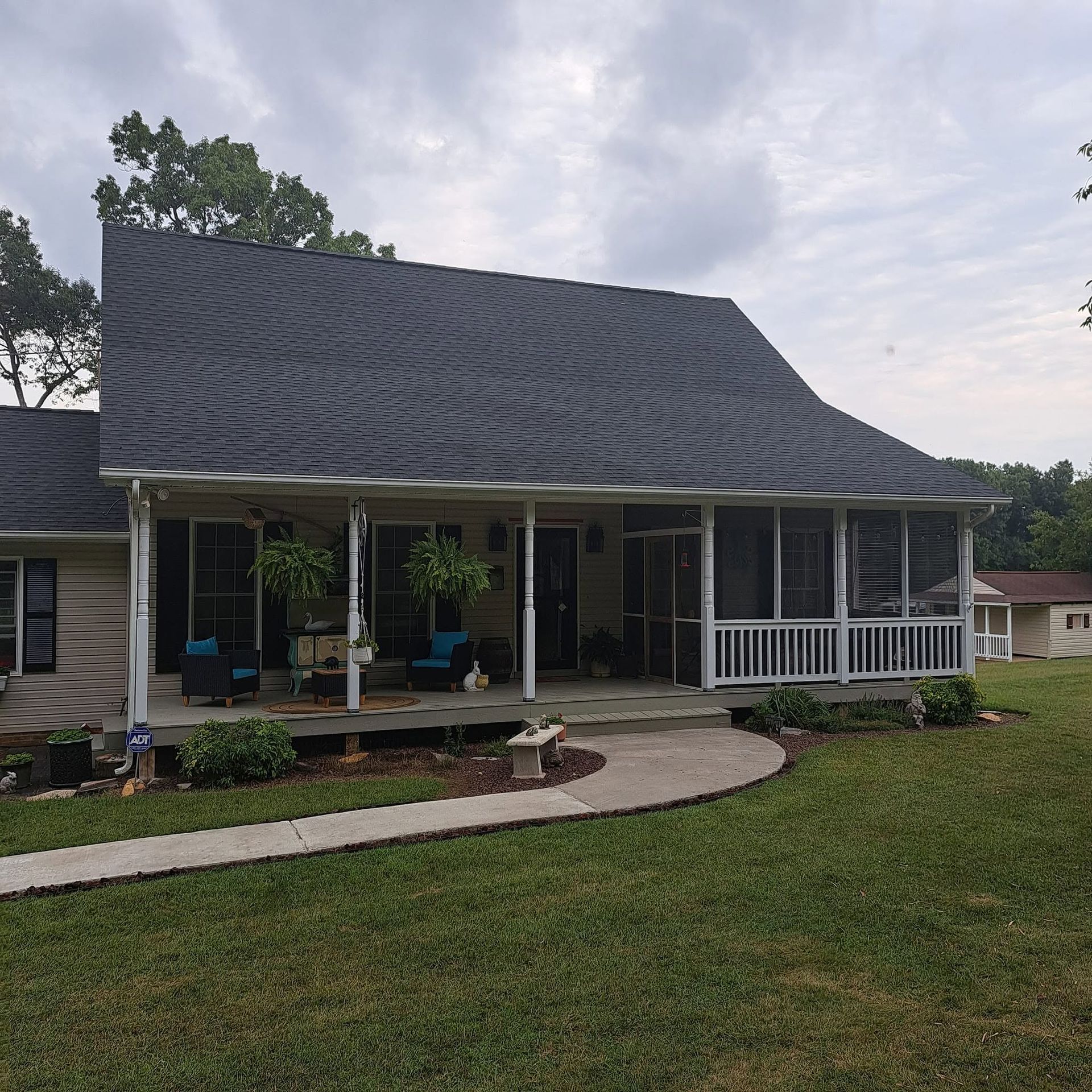 Small house with dark roof, front porch, curved walkway, and green lawn under a cloudy sky