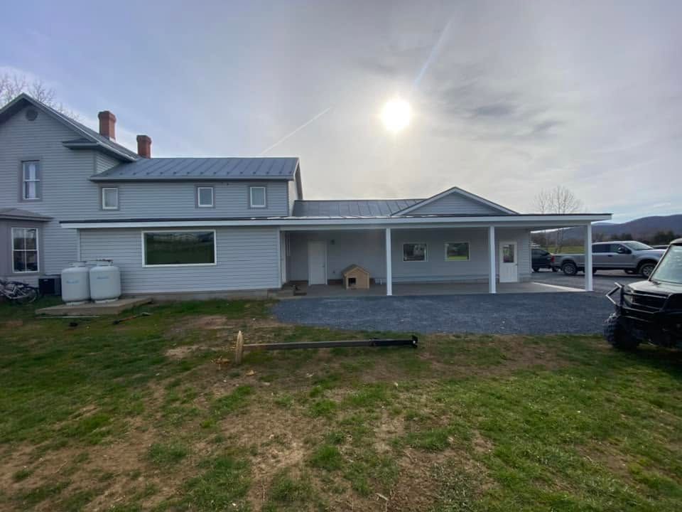 Suburban house with attached carport, driveway, and patchy front lawn under a bright sky