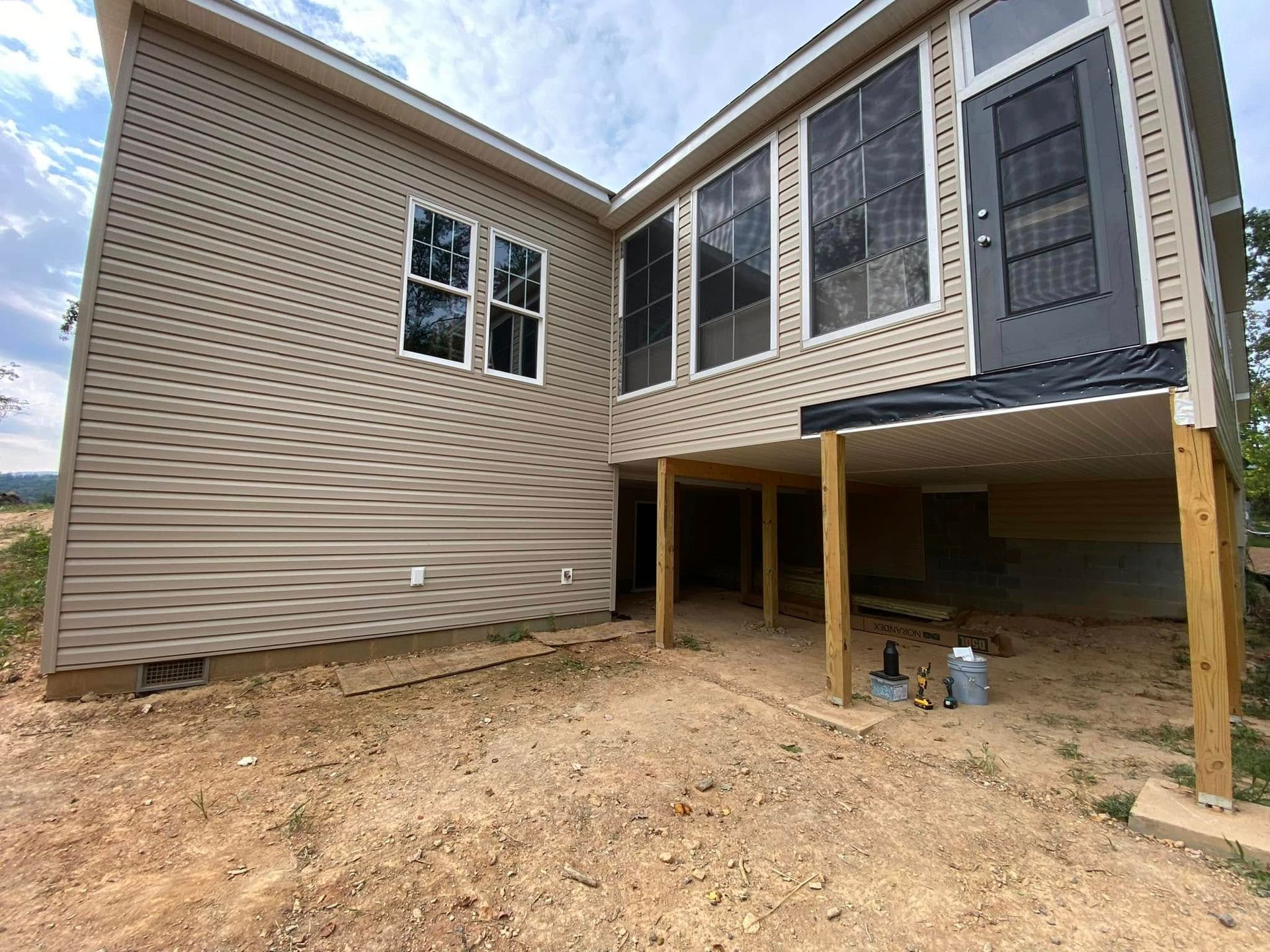 House exterior under construction with raised deck, beige siding, and exposed dirt yard
