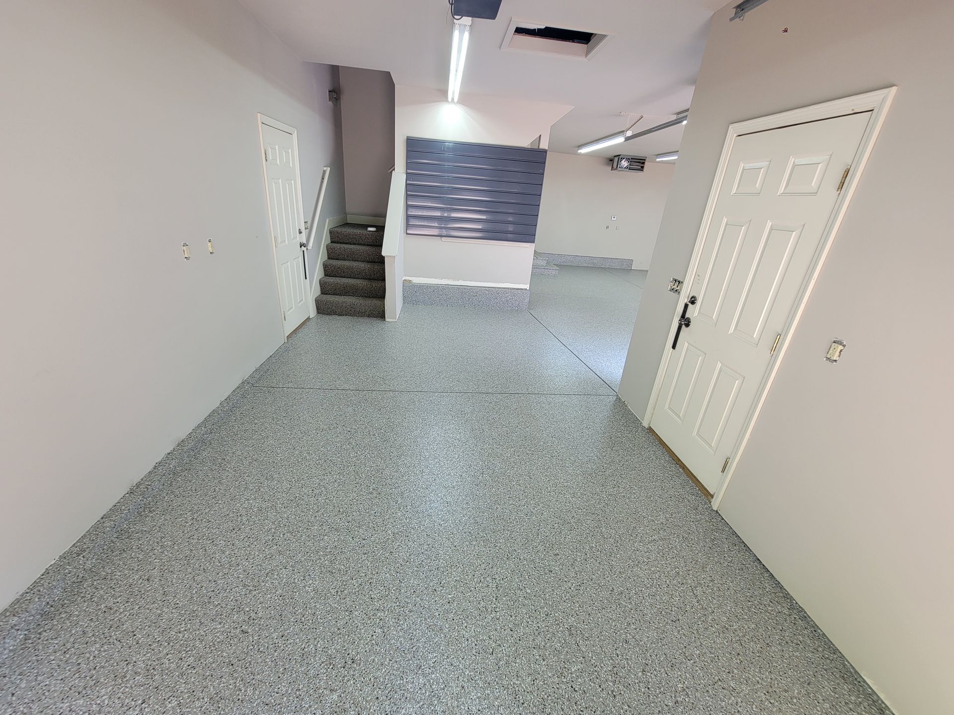 Empty office or hallway with white walls, speckled floor, stairs, and a closed door on the right.