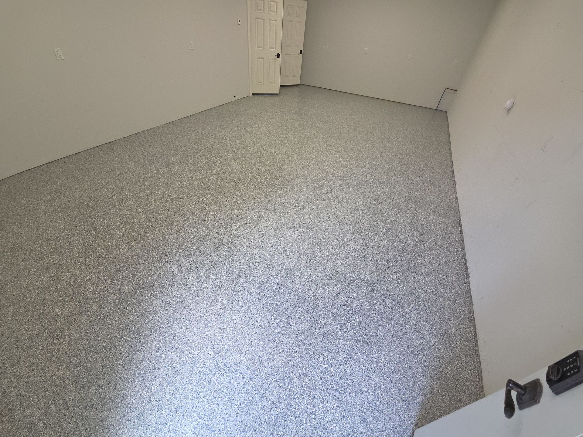 Empty white room with speckled gray floor and a small dark object in the lower-right corner