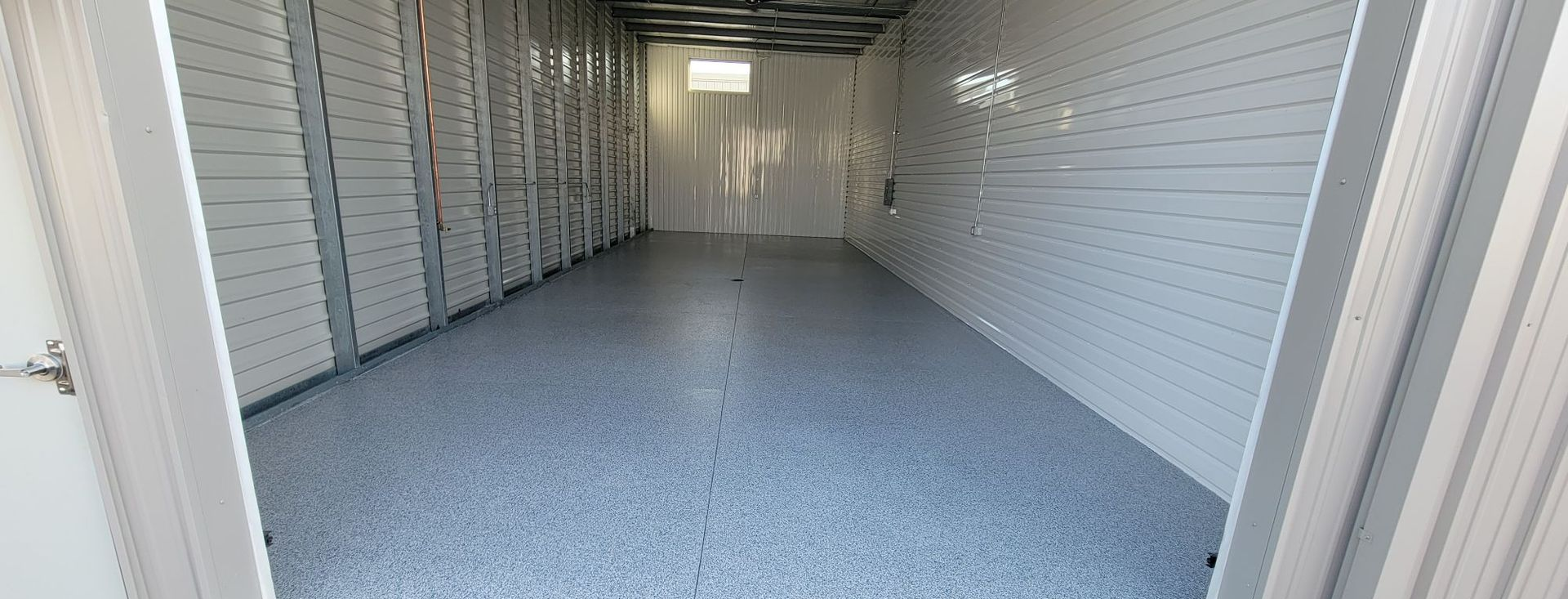 Open storage unit with white walls and gray speckled floor, viewed from the doorway