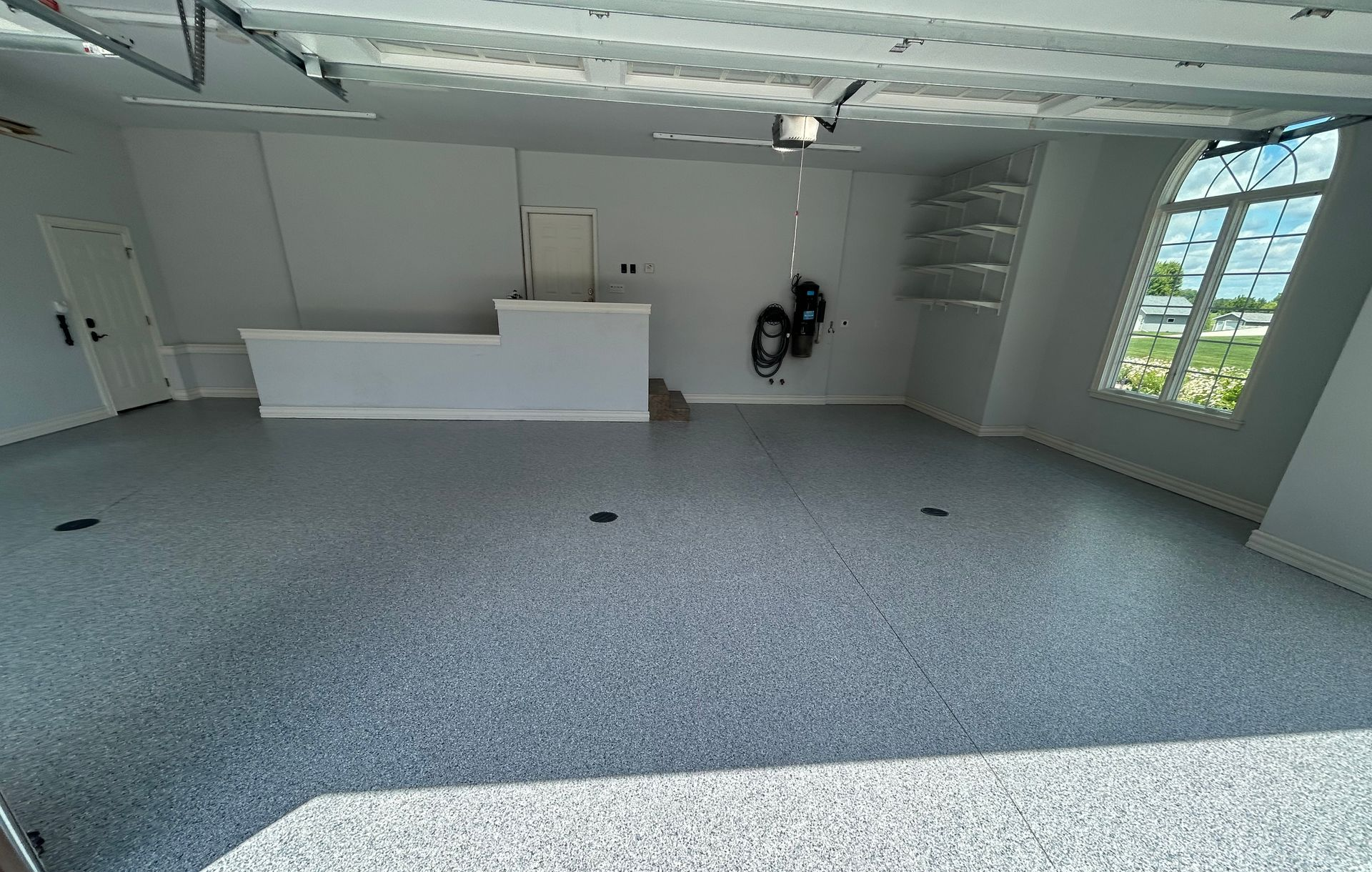 Empty gray-floored room with a white counter, ceiling fan, and windows on the right