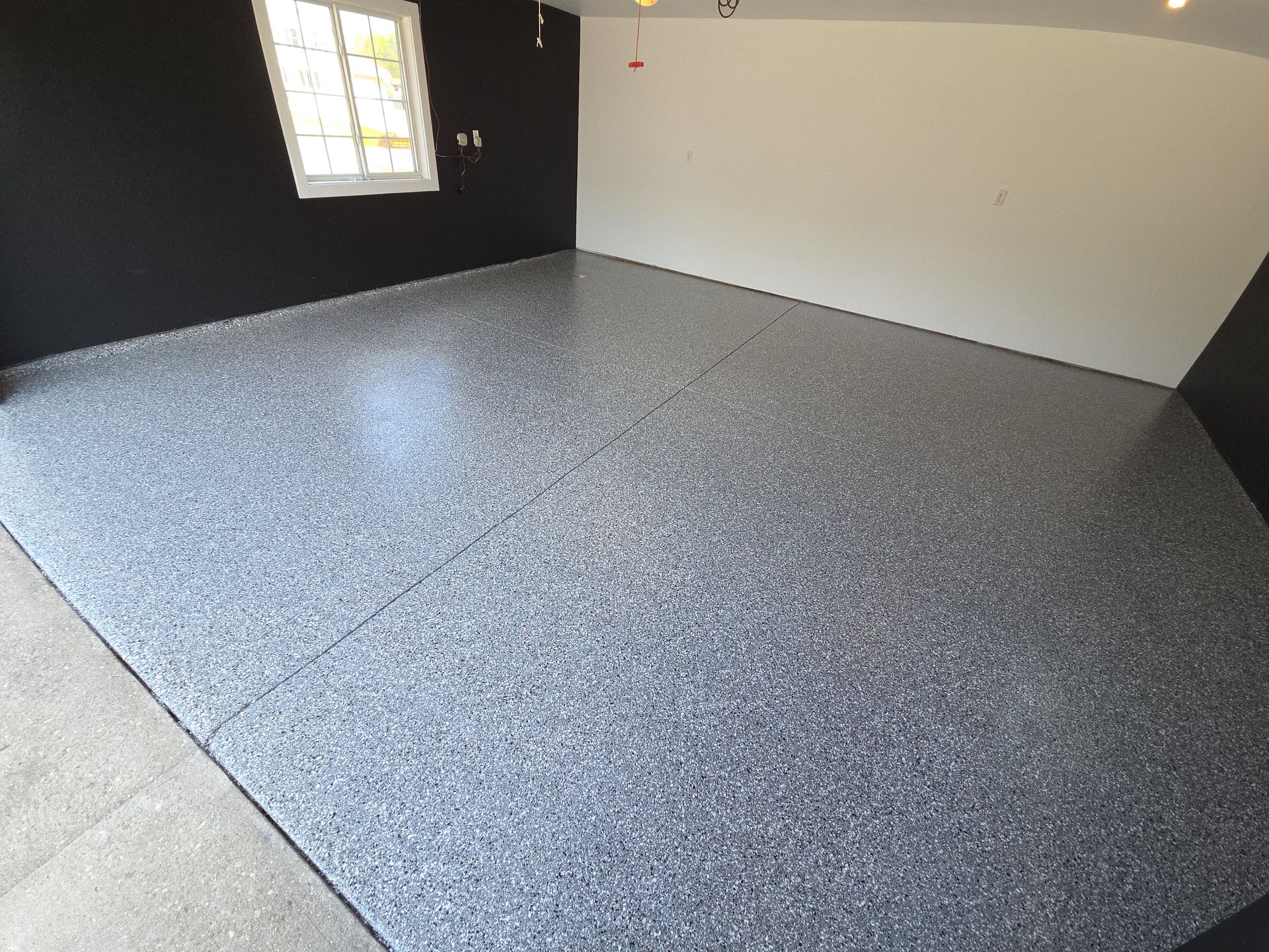 Empty room with gray speckled floor, white walls, and a small window on the left.