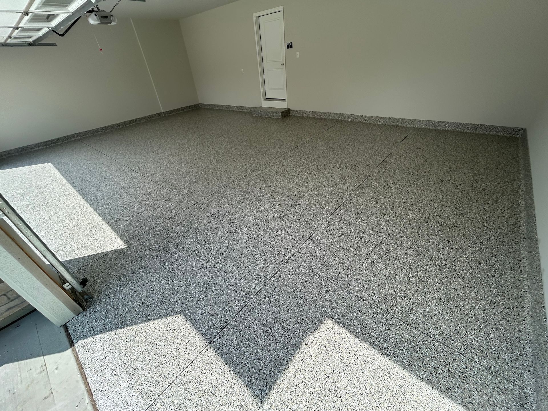 Empty gray-floored room with white walls, a door, and sunlight casting geometric shadows